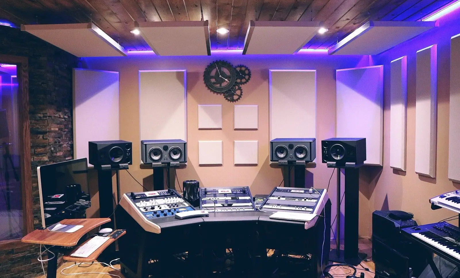 A recording studio with a mixing desk, four speakers and soft purple light